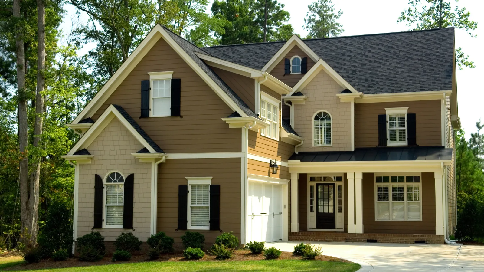 White garage door on a brown two-story house under a dark shingle roof