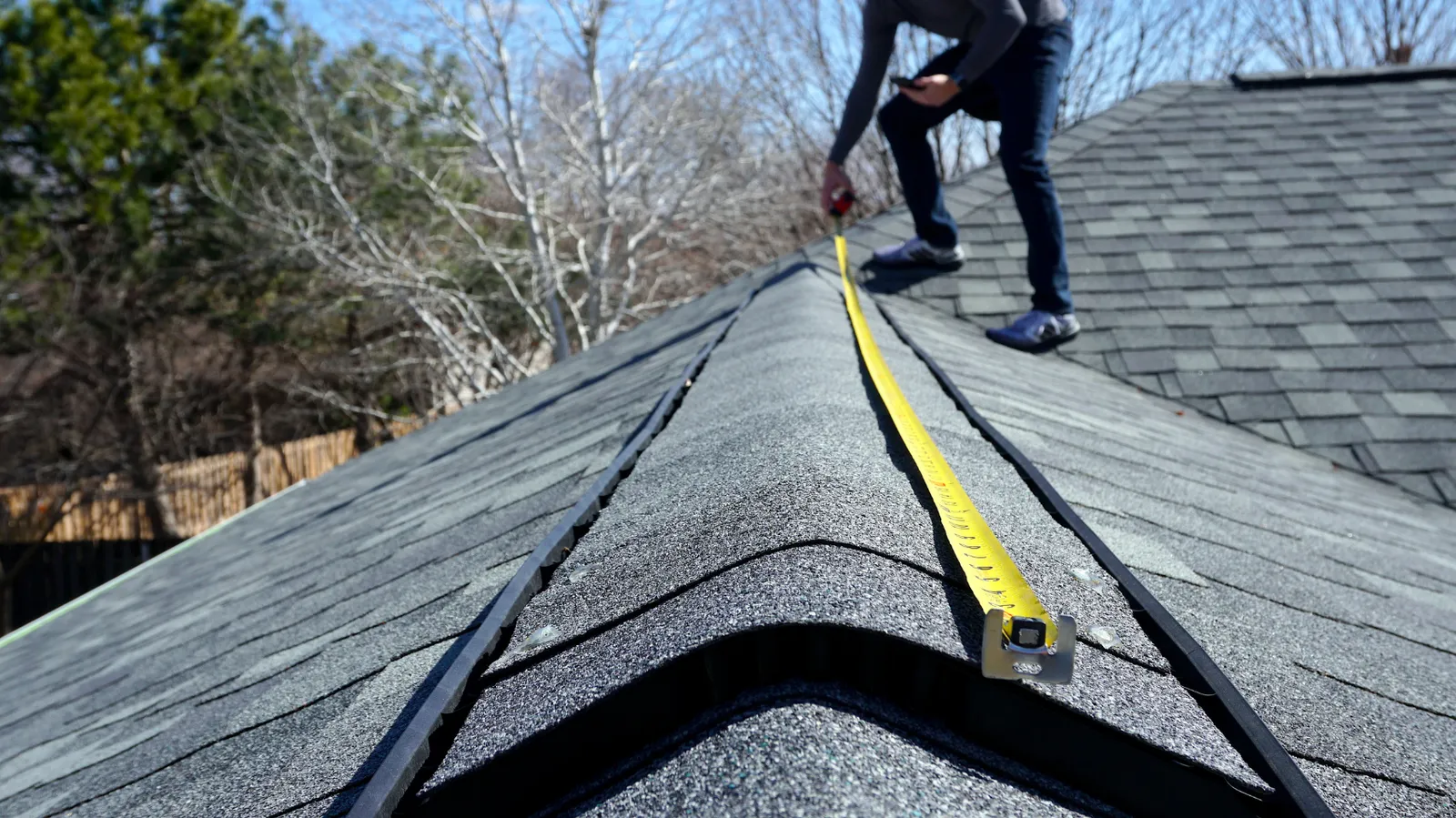 Shingle ridge being measured by a roofer with a tape measure
